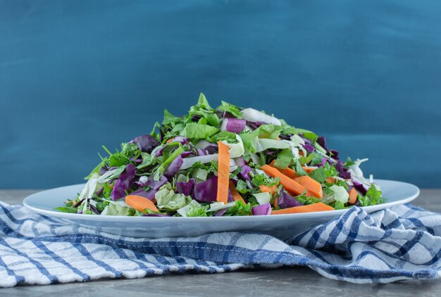 Salad prepared with fresh vegetables, on plate, on the towel , on the marble table. 