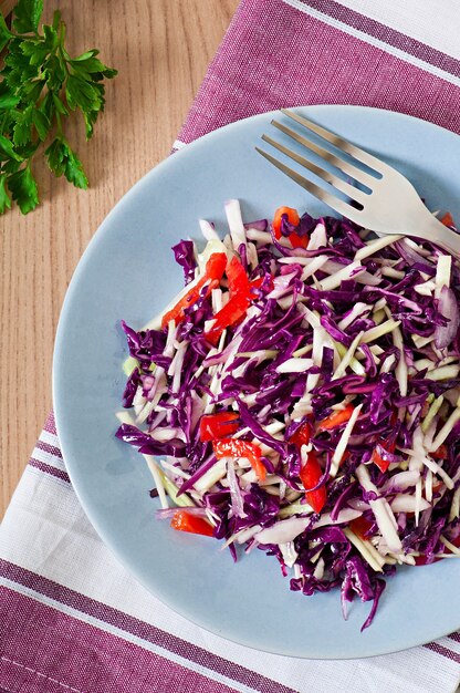 Salad of red and white cabbage and sweet red pepper, seasoned with lemon juice and olive oil in wooden bowl