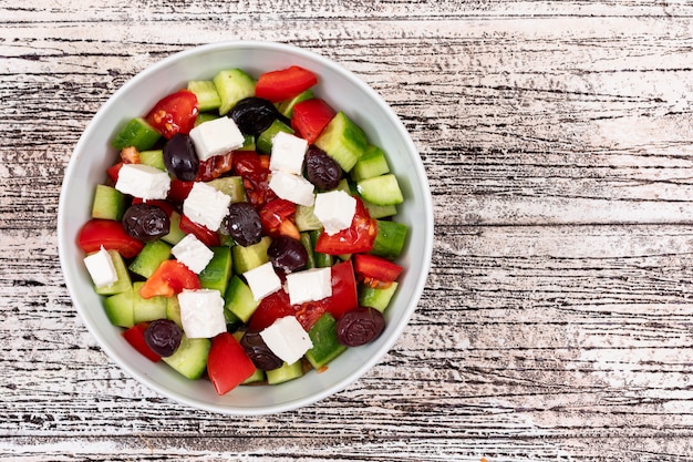 salad with cheese olive cucumber tomato in a white bowl on wooden table