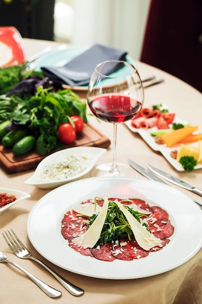 Free photo salad with pepperoni herbs and sliced parmesan with a glass of red wine.