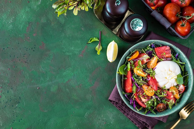 Free photo salad with tomatoes arugula burrata cheese and microgreens on a green stone background top view copy space