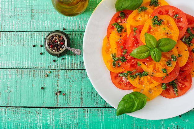 Salad of yellow and red tomato with Basil pesto on a light table. Flat lay. Top view