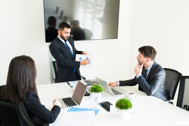 Sales are going up in the company. Attractive sales representative showing a graph with the business goals to his co-workers in the meeting room