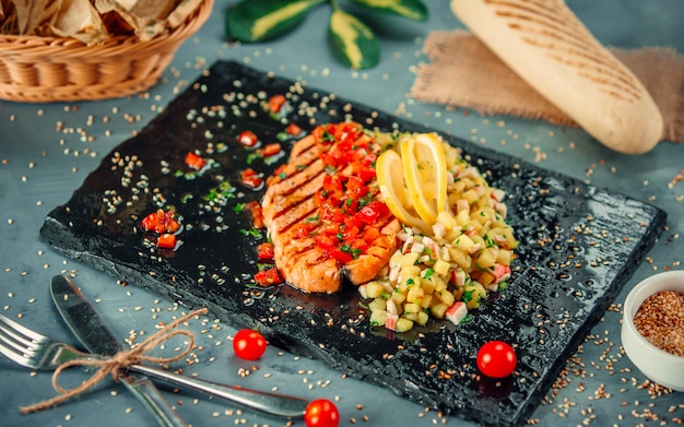 Free photo salmon steak with lemon and vegetable salad on a black stone platter.