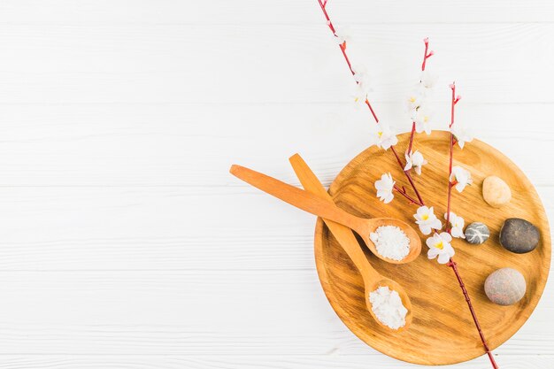 Salt spoon; flowers and spa stone on wooden board over white surface