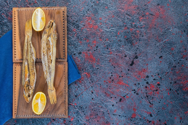 Free Photo salty dried fish with a slice of lemon isolated on a wooden board 