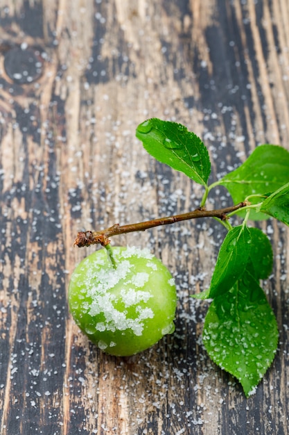 Salty green plum with branch high angle view on a wooden wall