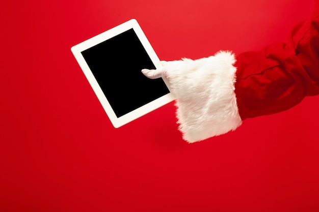 Free photo santa claus holding laptop ready for christmas time on red studio background. the season, holiday, celebration, gift concept