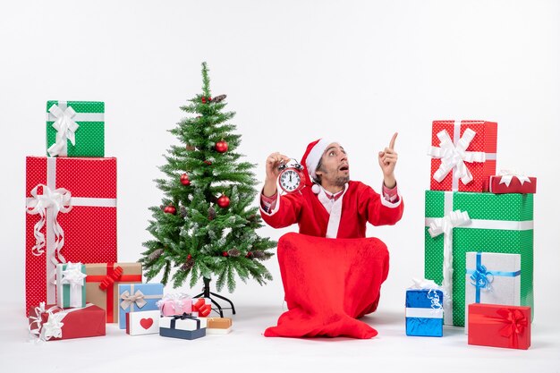 Santa claus pointing above sitting with gift boxes and tree