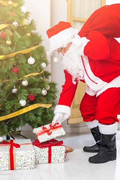 Free photo santa claus putting presents under fir tree