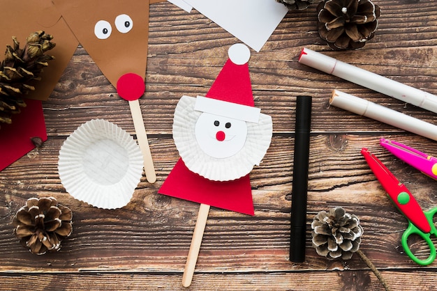 Free photo santa claus and reindeer props with pinecones; felt-tip pen and scissor on wooden desk