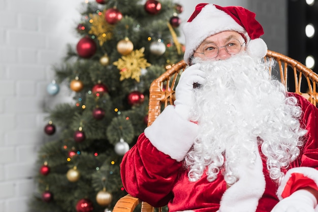 Free photo santa claus sitting on chair and talking by phone