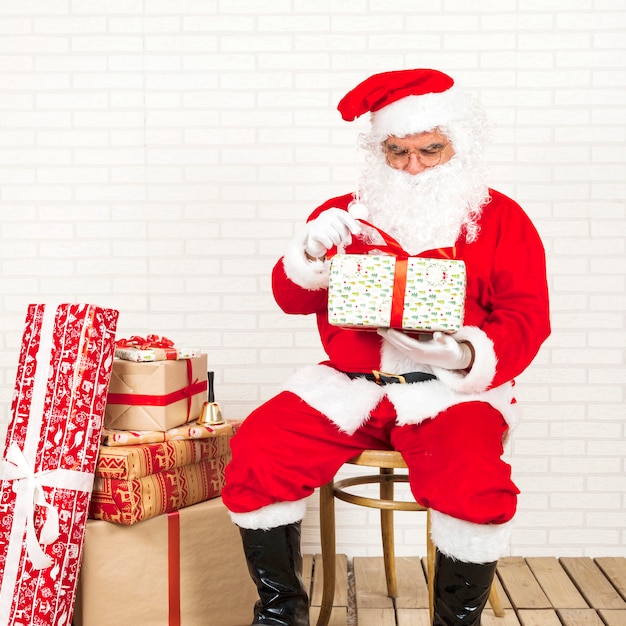 Free photo santa claus sitting and holding present in hands