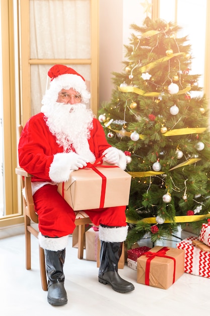 Free Photo santa claus sitting near christmas tree with present