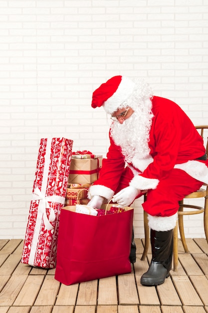 Free Photo santa claus sitting and putting presents in paper bag