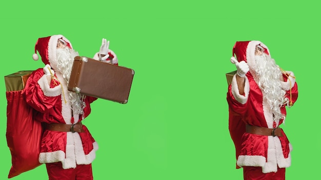 Free photo santa hitchhiking with suitcase and sack full of gifts for children, making signs for transportation over greenscreen. saint nick carrying briefcase and presents in iconic red bag.