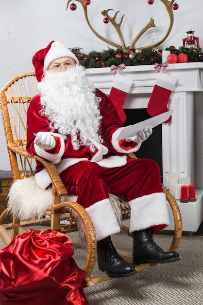 Free photo santa sitting in rocking chair with wishlist