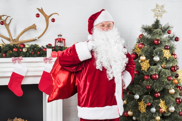 Santa with big sack of gifts near Christmas tree