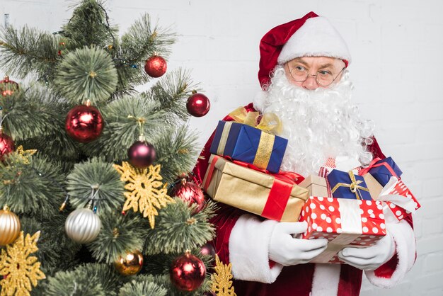 Santa with gift boxes in hands near decorated Christmas tree