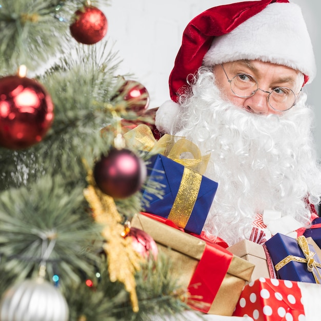 Santa with presents in hands near Christmas tree