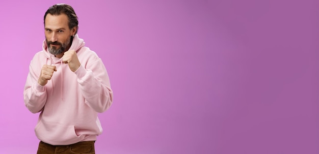 Free Photo sassy confident goodlooking mature caucasian bearded man in pink hoodie teaching son how stand back fight defend himself raise fists ready boxing smiling daring stay good shape purple background