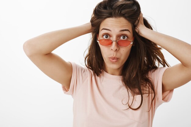 Sassy girl with sunglasses posing against the white wall