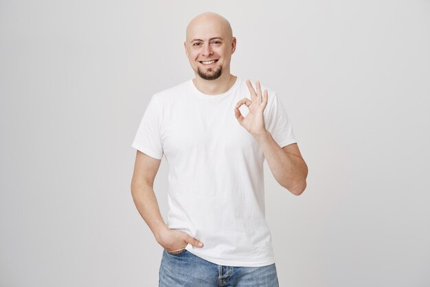 Satisfied bald bearded man in white t-shirt show okay sign, approve