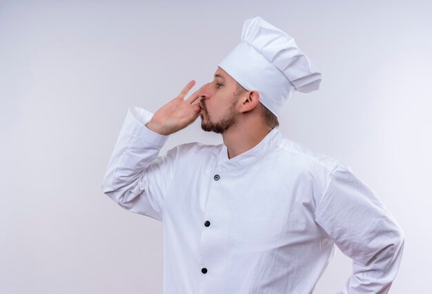 Satisfied professional male chef cook in white uniform and cook hat showing sign for delicious standing over white background