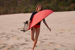 Free photo satisfied surfing young woman holds surfboard, spends summer holidays on tropical island