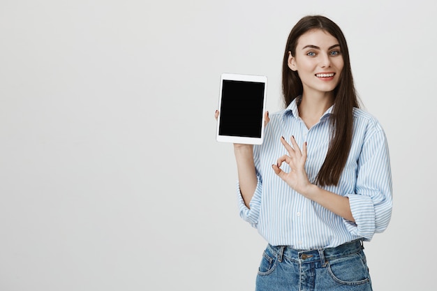 Satisfied woman showing digital tablet and okay sign