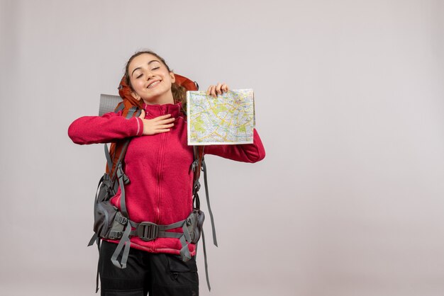 satisfied young traveller with big backpack holding map on grey