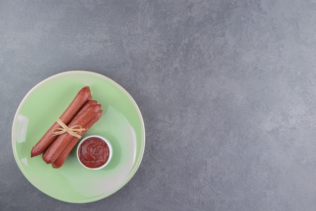 Sausages tied up and ketchup on the plate, on the marble surface