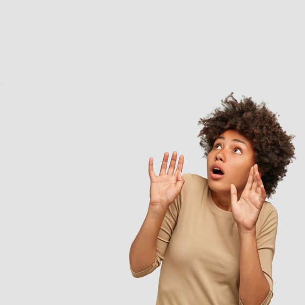 Scared dark skinned young African female keeps hands in protective gesture