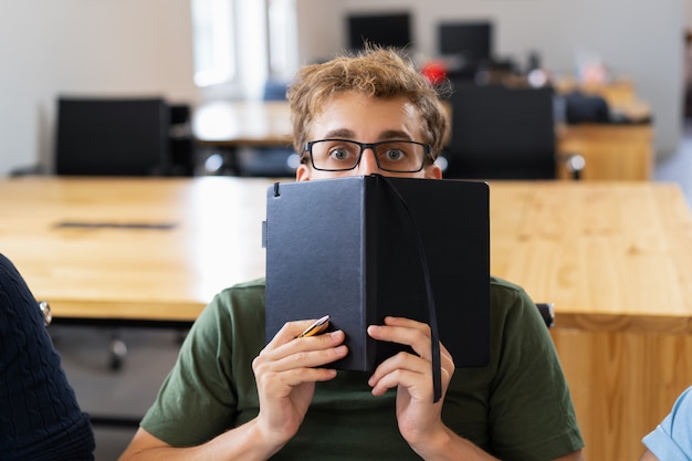 Free photo scared male student hiding behind notebook