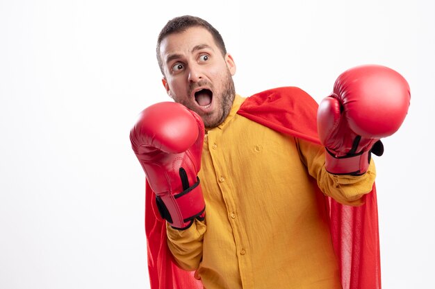 Scared superhero man stands with boxing gloves isolated on white wall