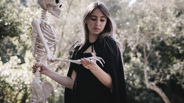 Free photo scared woman in wizard clothes holding skeleton