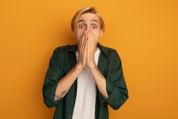 Free photo scared young blonde guy wearing green t-shirt covered face with hands