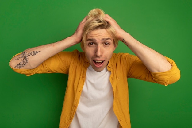 Free photo scared young blonde guy wearing yellow t-shirt grabbed head isolated on green