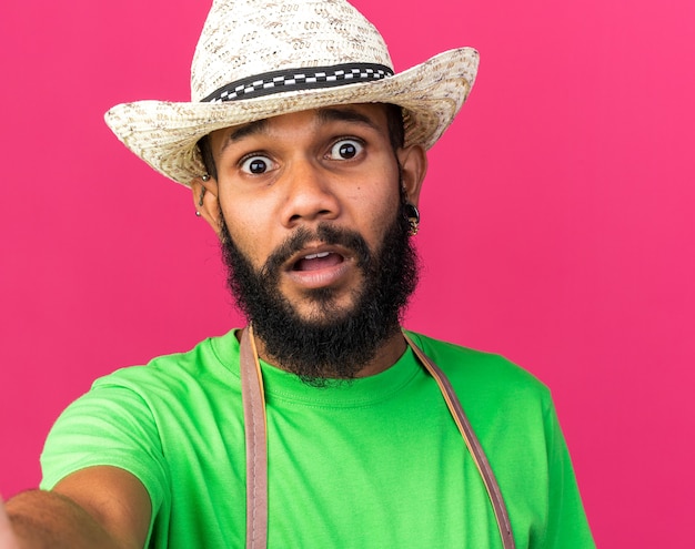 Free photo scared young gardener afro-american guy wearing gardening hat holding camera