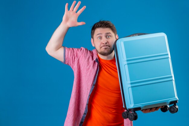 Free Photo scared young handsome traveler man holding suitcase raising hand