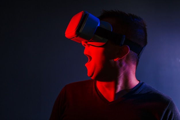 Scared young man in vr 3d glasses on dark background with red blue lighting