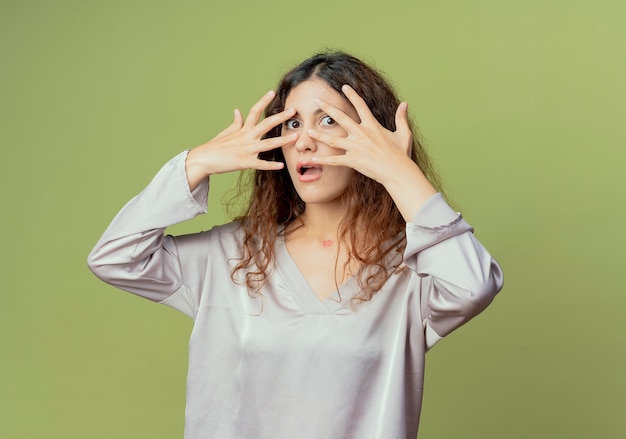 Scared young pretty female office worker covered face with hands isolated on olive green