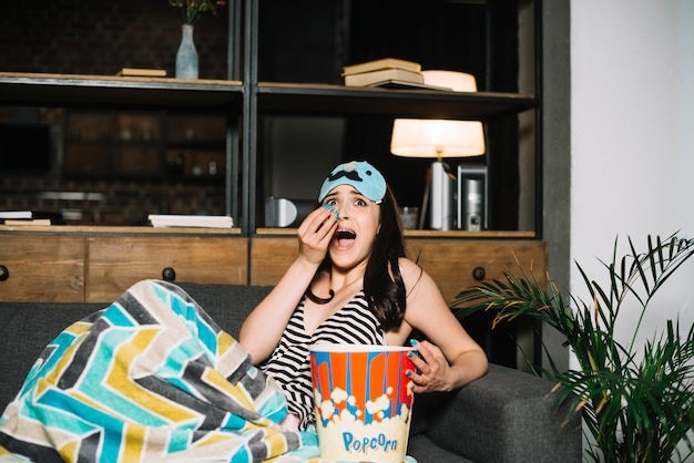 Free photo scared young woman sitting on bed with popcorn