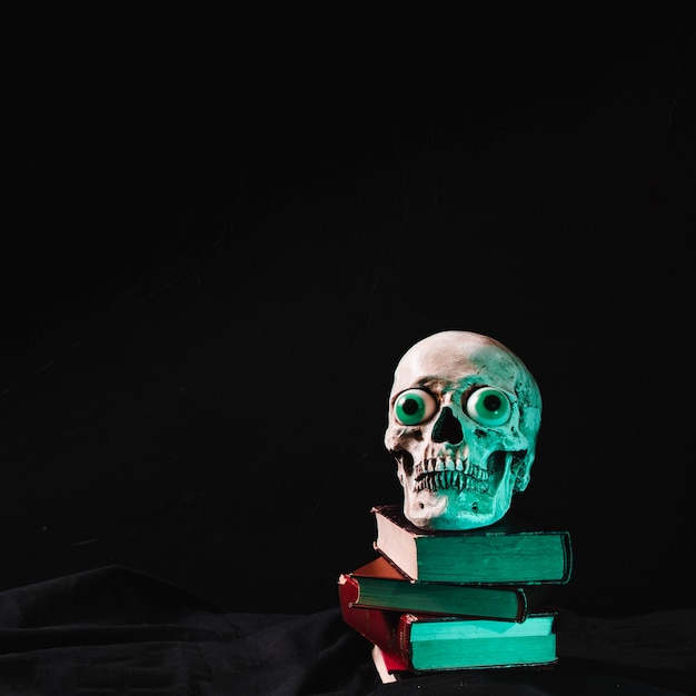 Scary skull with fancy eyes lying on pile of books