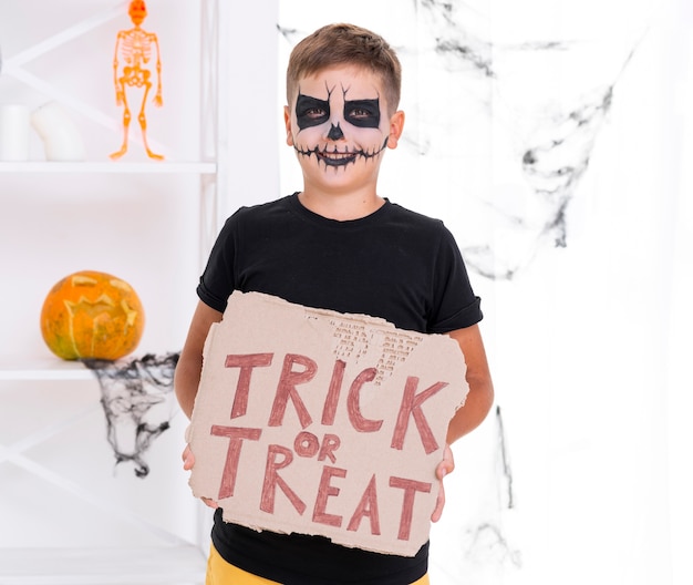 Free Photo scary young boy holding trick or treat sign