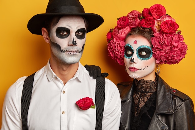 Free photo scarying zombie girl leans at shoulder of man, looks attentively, serious man wears black hat, white shirt with suspenders, prepare for halloween celebration.