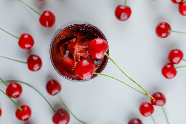 Scattered cherries with icy drink, flat lay.