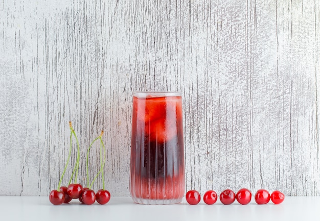 Free Photo scattered cherries with icy drink on white and grungy table, side view.