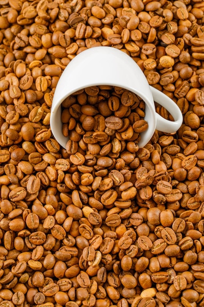 Scattered coffee beans in a white cup . high angle view.