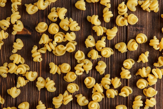 Scattered dry pasta on wooden table, flat lay.